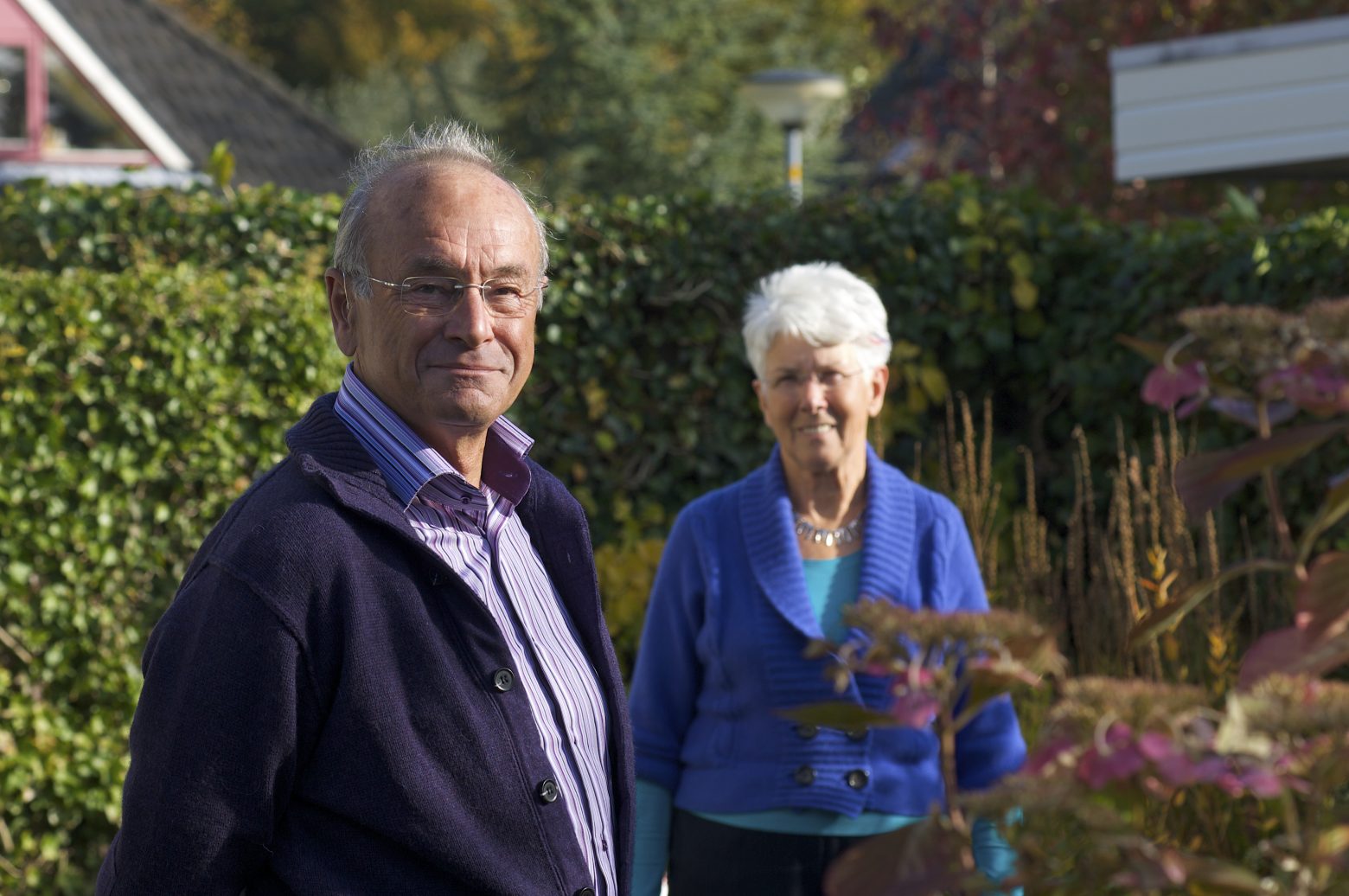 Twee oudere mensen staan in een tuin
